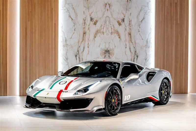 A silver Ferrari 488 Pista with Italian flag racing stripes and the number 10 displayed, parked indoors against a marble and wood backdrop—a true track-ready Ferrari that commands attention.