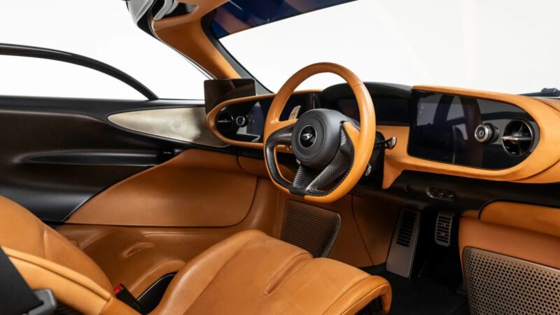 Interior view of an ultra-low mile McLaren Speedtail with $250k in MSO options, featuring tan leather seats, a matching steering wheel, and multiple digital display screens on the dashboard.