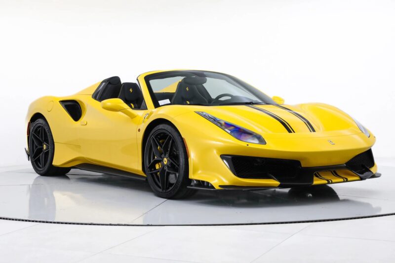 A track-ready yellow Ferrari 488 Pista convertible sports car with black racing stripes is parked in a white studio setting.