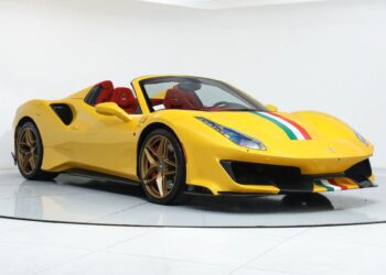 A yellow Ferrari 488 Pista with red interior, gold wheels, and green, white, and red racing stripes is displayed in a white showroom, highlighting this stunning track-ready Ferrari for sale.