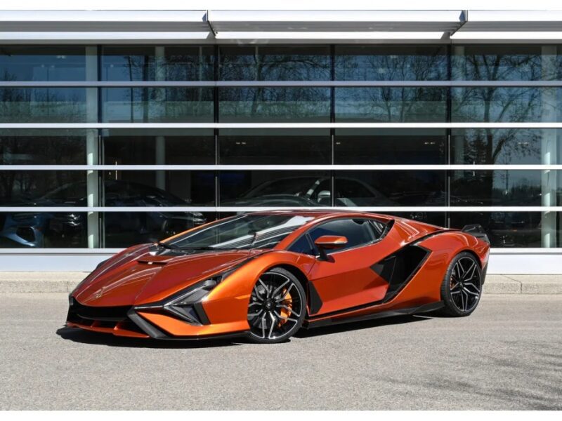 An orange Lamborghini luxury car is parked on a paved surface in front of a modern glass building.