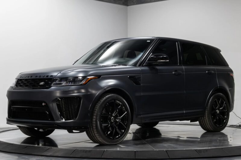A dark gray Range Rover Luxury SUV with black wheels is parked in a white indoor studio on a rotating display platform.
