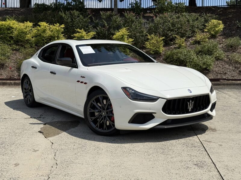 A white Maserati sedan, epitomizing Italian luxury, is parked outdoors on a sunny day, surrounded by greenery and a paved surface.