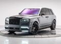 The Rolls-Royce Cullinan, a luxury SUV with a matte silver and black finish, large black wheels, tinted windows, and LED headlights, is elegantly displayed in a studio setting on a rotating platform.