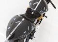 A top-down view of a modern 2022 Aston Martin AMB 001 motorcycle with a carbon fiber body, black seat, yellow suspension spring, and minimalist handlebars on a white tiled floor—an exclusive offering from Sotheby's Motorsport.