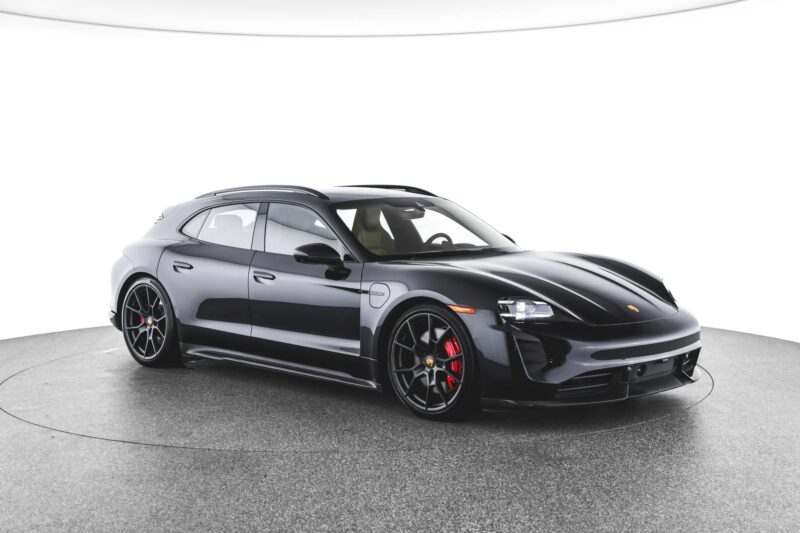 A black Porsche Taycan Cross Turismo, one of the finest luxury performance wagons, is displayed in a well-lit studio with a white background, viewed from the front left side.