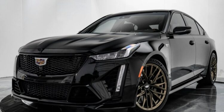A black Cadillac sedan with bronze wheels, known among the best manual transmission cars, is parked indoors on a glossy black platform, facing slightly left.