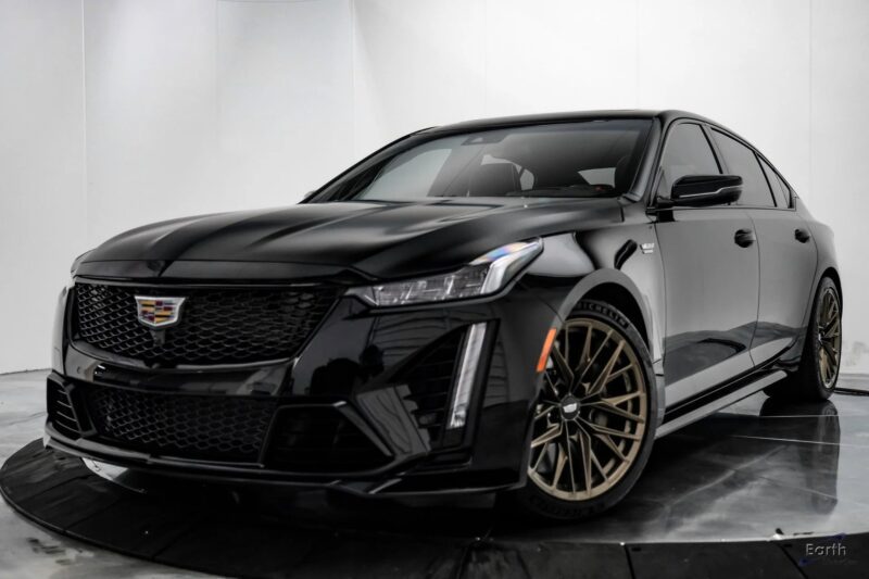 A black Cadillac sedan with bronze wheels, known among the best manual transmission cars, is parked indoors on a glossy black platform, facing slightly left.