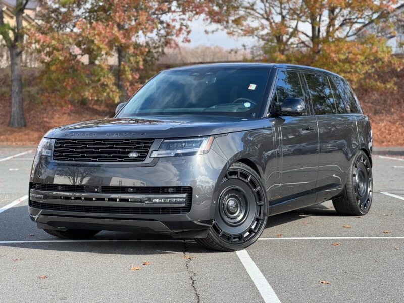 A gray Range Rover, one of the best luxury SUVs, is parked in an outdoor lot surrounded by autumn trees and fallen leaves.