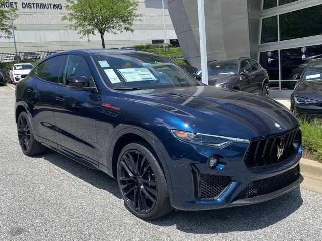 A blue Maserati Levante SUV, an icon of Italian luxury, is parked outside a modern building with information sheets on the windshield, indicating it is for sale.