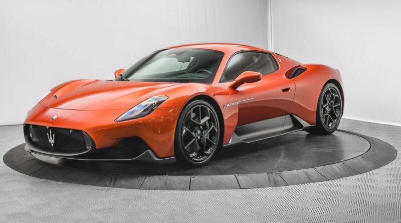 A red Maserati sports car, epitomizing Italian luxury, is parked in a white, well-lit studio on a circular platform.