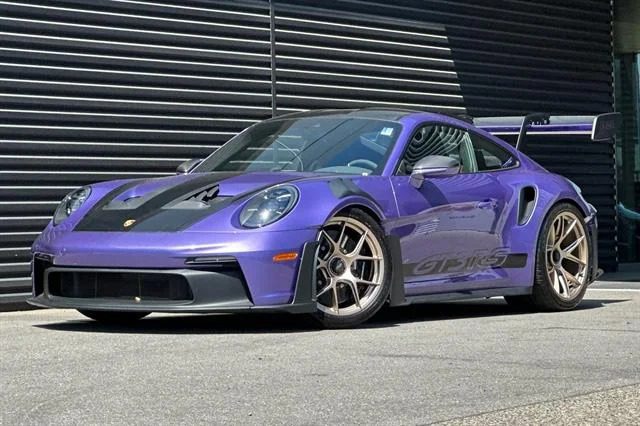 A high-performance, paint-to-sample Porsche 911 GT3 RS in striking purple is parked in front of a building with black horizontal metal siding.