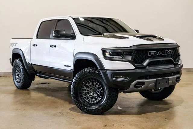 A white Ram TRX pickup truck with black accents and large off-road tires, this luxury car stands out among cars for sale, parked indoors on a concrete floor.