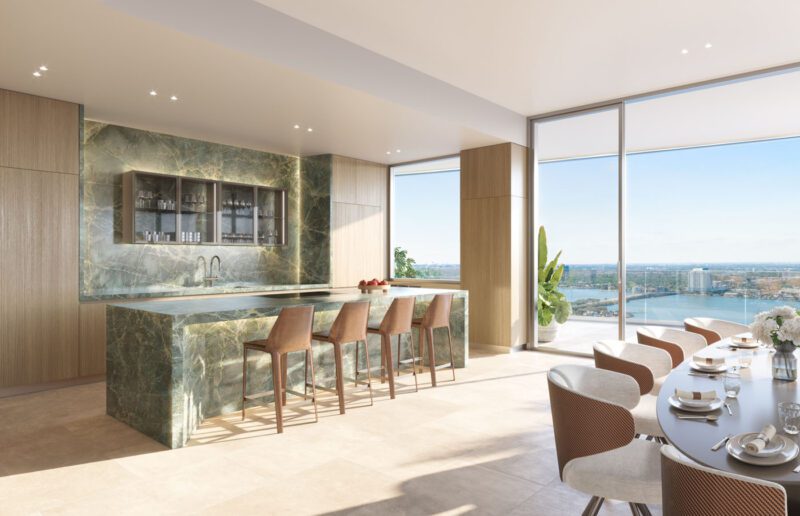 Modern kitchen with a green marble island, wooden cabinets, bar stools, and a dining area by floor-to-ceiling windows overlooking a cityscape and river.