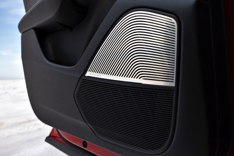 Close-up of a 2025 Audi SQ8 car door interior, showcasing a speaker grille with a metallic, lined design and a textured black lower section.