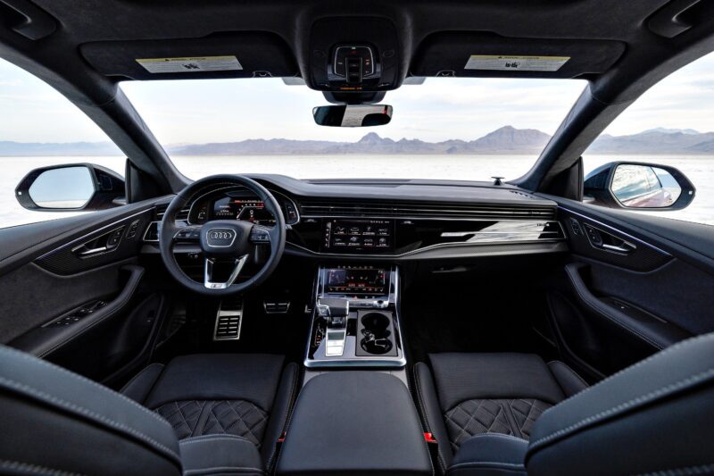 Interior view of the 2025 Audi SQ8 showcasing its sleek dashboard, sporty steering wheel, center console, and front seats, with a desert landscape visible through the windshield.