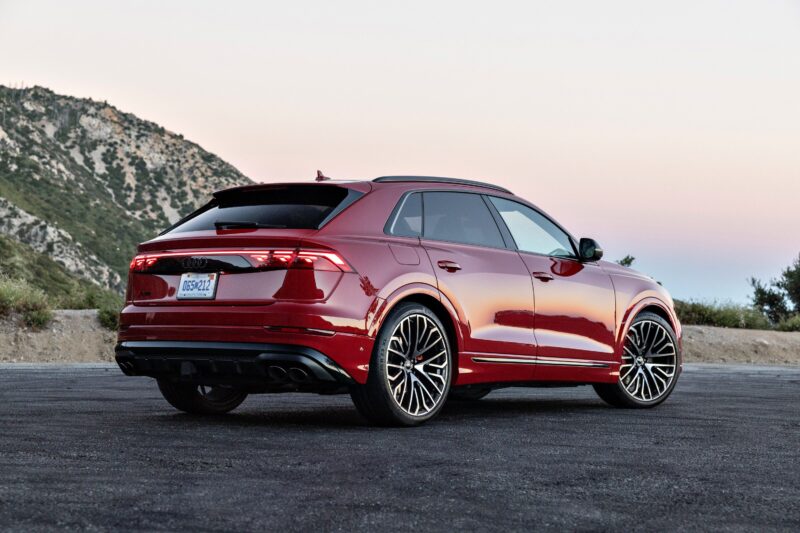 A red 2025 Audi SQ8 is parked on a paved surface near a mountain at sunset, viewed from the rear three-quarter angle—an impressive sight for any Audi SQ8 review.