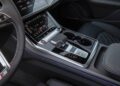 Close-up of a modern car interior, as seen in the Review: 2025 Audi SQ8 Combines Style With Substance, showing the center console with digital touchscreens, gear shifter, climate controls, cup holders, and leather upholstery.