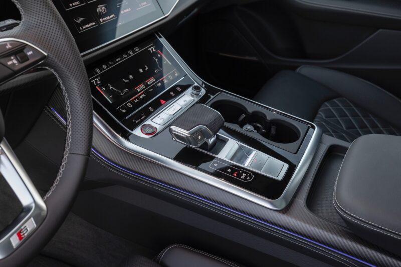 Close-up of a modern car interior, as seen in the Review: 2025 Audi SQ8 Combines Style With Substance, showing the center console with digital touchscreens, gear shifter, climate controls, cup holders, and leather upholstery.