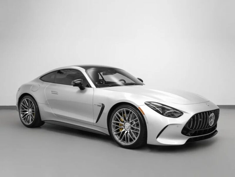 A silver two-door luxury car with black accents, large alloy wheels, and a sleek aerodynamic design, parked indoors against a plain light background.