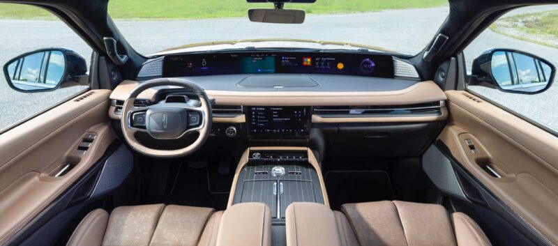 The interior of a modern car featuring a digital dashboard, touchscreen controls, tan leather seats, and a panoramic windshield view offers the spa-like luxury found in the Review: 2025 Lincoln Navigator L Black Label Coddles Like A Spa On Wheels.