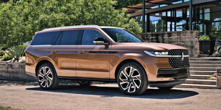 A bronze Lincoln Navigator SUV is parked on a gravel driveway in front of modern steps and greenery on a sunny day, echoing the comfort described in the Review: 2025 Lincoln Navigator L Black Label Coddles Like A Spa On Wheels.