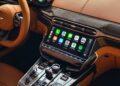 Close-up of a 2026 Aston Martin Vanquish interior, featuring a touchscreen display with Apple CarPlay interface, surrounded by brown leather and carbon fiber trim—perfectly complementing its powerful V12 engine.
