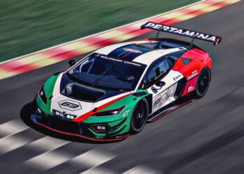 A Lamborghini race car with a green, white, and red livery speeds on a race track. The car features sponsor logos and a large rear wing.