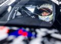 A race car driver wearing a helmet sits inside a Next-Gen Porsche 911 Cup Car, visible through the windshield, gearing up for the 2026 Race Season.