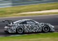 A next-gen sports car with black and white camouflage wrap, possibly the upcoming Porsche 911 Cup for the 2026 race season, speeds along a racetrack, captured in motion against a blurred background.