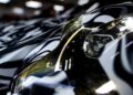 Close-up of a Porsche 911 Cup Car headlight and side mirror on a vehicle with a black and white camouflage wrap; hints at next-gen features for the 2026 race season, with "Porsche" visible on the headlight.