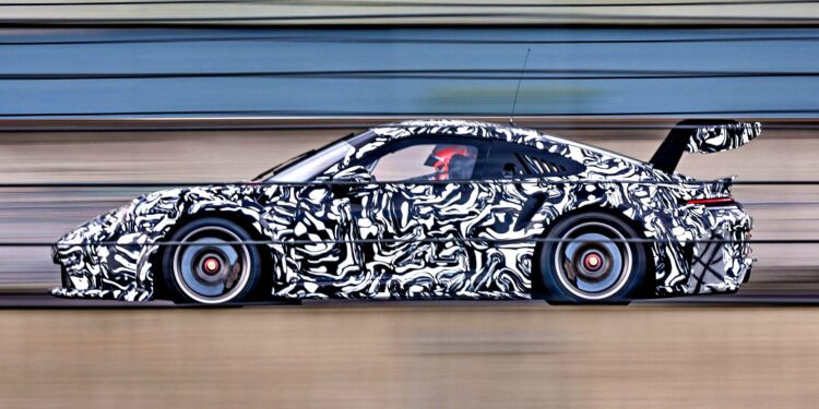 A next-gen race car with black-and-white camouflage wraps speeds along a track, motion blur highlighting its pace, and a large rear wing visible—hinting at innovations for the 2026 race season.