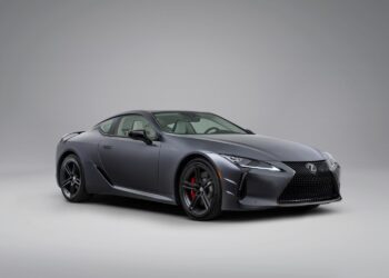 A matte gray Lexus coupe is parked in a studio with a plain light gray background, viewed from the front left angle.