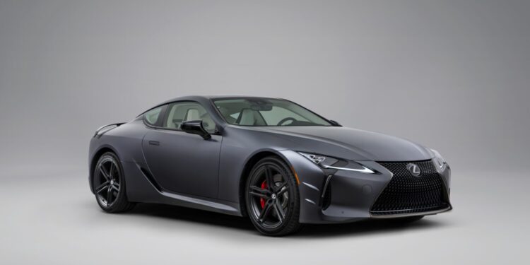 A matte gray Lexus coupe is parked in a studio with a plain light gray background, viewed from the front left angle.