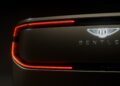 Close-up of the rear end of a Bentley EV, showing the illuminated Bentley logo and BENTLEY lettering, with striking red LED tail lights visible on a dark background.