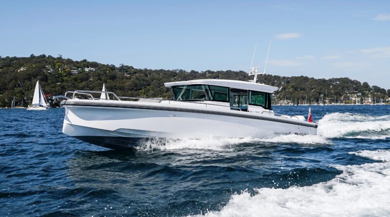 A white motorboat travels across choppy blue water, offering a true maritime experience, with a tree-lined shoreline and several sailboats in the background.