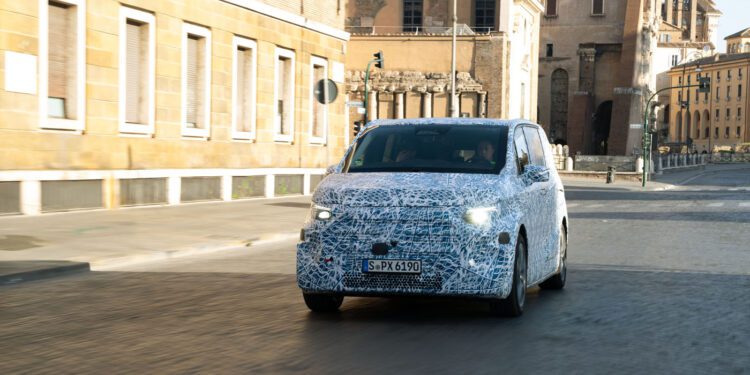 A camouflaged Mercedes-Benz prototype, possibly the VLE Electric Van, with a German license plate is being tested on a city street in Rome, with historic buildings in the background.