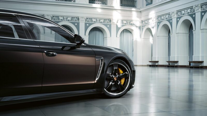 A black Porsche luxury sports car, crafted for exclusive customer requests, is parked indoors in a spacious, elegant hall with white columns and arched windows.