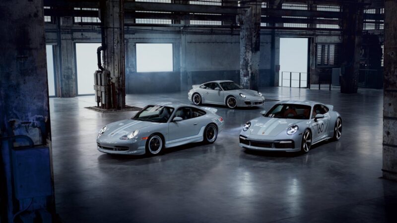 Three Porsche 911 sports cars, including rare factory one-off cars built for exclusive customer requests, are parked in an industrial warehouse with concrete floors and large windows.
