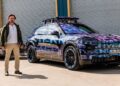 A man stands next to a camouflaged Porsche SUV, reminiscent of something Richard Hammond might drive, parked in front of a large industrial garage door.