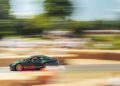 A green Porsche GT3 sports car speeds down a racetrack with motion blur in the background and barriers on each side, capturing the thrilling world of race cars.