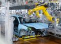 A yellow robotic arm assembles a partially built blue Porsche Macan on an automated production line in a modern automotive factory, celebrating the production of its millionth unit.