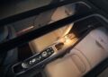 Interior view of a Bentley electric car seen from above, showcasing two beige seats, a central control console, and ambient lighting streaming through the panoramic glass roof.