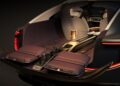 Open trunk of a Bentley EV concept reveals two fold-out seats, a central table with a bottle and glasses, plus ambient lighting, all viewed elegantly from the rear.