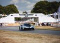 A Zenvo Aurora sports car, boasting 850HP, drives on the track at the Goodwood Festival of Speed during its global debut, with spectators and event banners visible in the background.