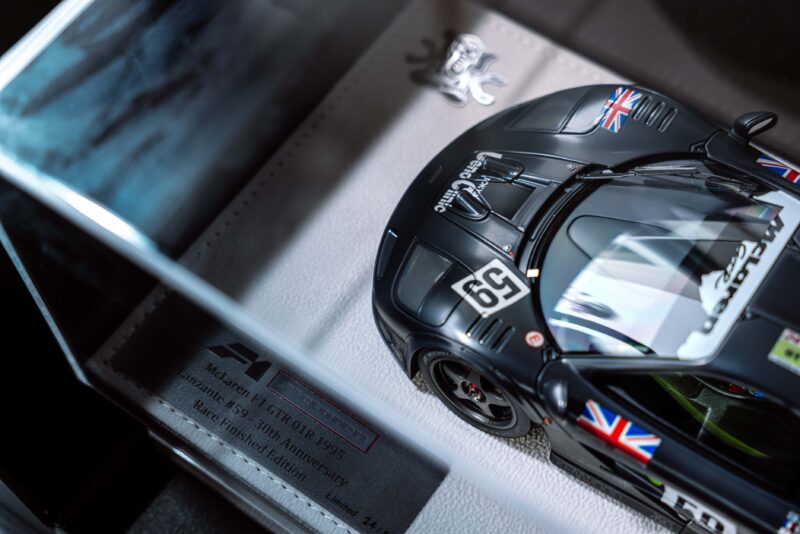 Close-up of a black McLaren F1 GTR model race car with UK flags and the number 59, displayed in a case with a plaque marking the 30th anniversary of Le Mans and F1 Limited Edition status by Lanzante at Goodwood.