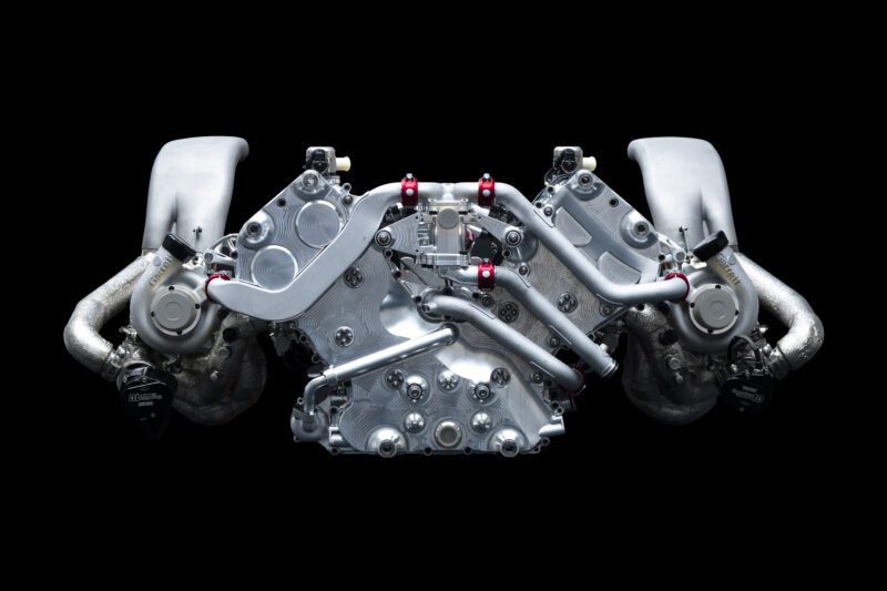 A high-performance V8 Twin-Turbo engine is displayed against a black background, showcasing metallic components and dual intake systems inspired by the GMR‑001 Hypercar from Genesis Magma Racing.