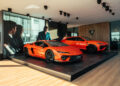 Two orange Lamborghini Temerario cars are displayed on a platform inside a modern showroom with large video screens and wood panel accents, capturing the spirit of Goodwood's automotive excellence.