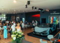 A crowd gathers inside a modern showroom at Goodwood, featuring a Lamborghini sports car on display and a wall of Temerario color samples.