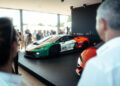 A Lamborghini Temerario race car with a striking green, white, and red livery is displayed on a platform indoors at Goodwood, drawing the attention of people viewing the exhibition.